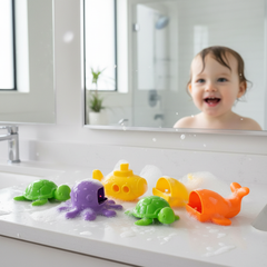 Colorful take-apart bath toys being disassembled for cleaning in a bright bathroom, with a toddler in the background.